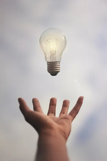 Eine Glühbirne, die über einer Hand schwebt.